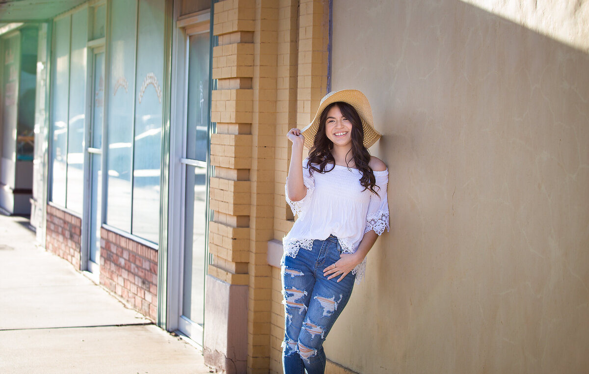 Senior girl with sun hat standing against wall in downtown plainview tx