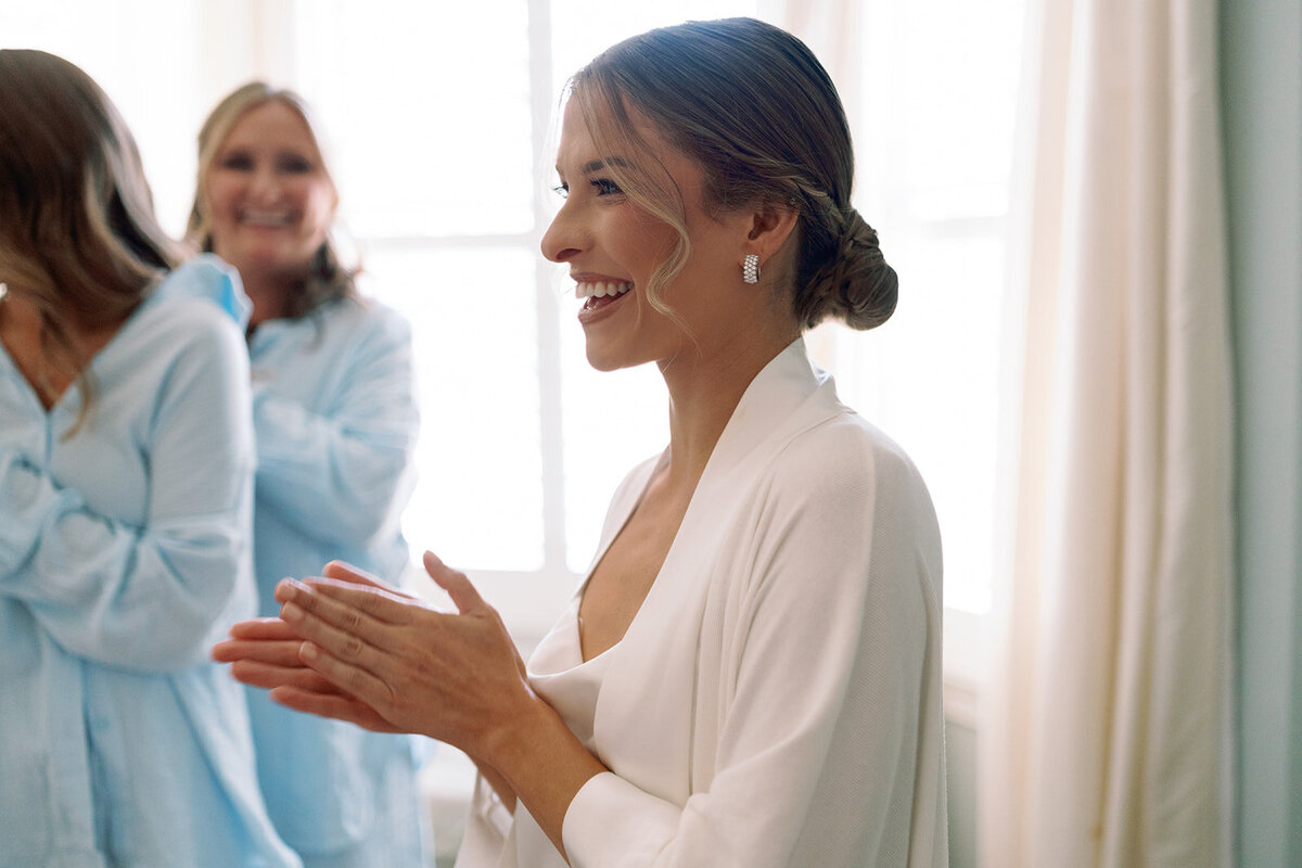 Bride smiling and clapping her hands while getting ready on her wedding day at Burritt on the Mountain in Huntsville, Alabama, captured by Perry Hancock.