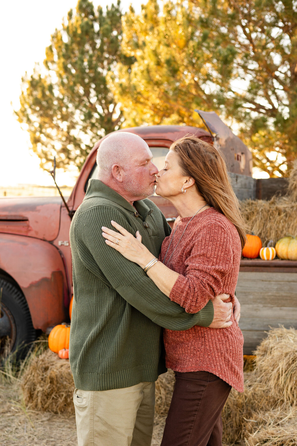 Husband and wife stand in front of a vintage red farm truck and share a kiss.