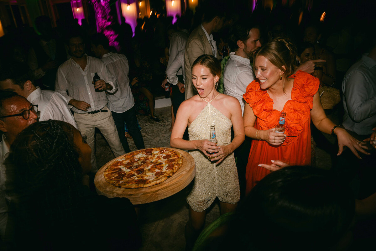 A bride being presented with a pizza on the dance floor at her wedding.