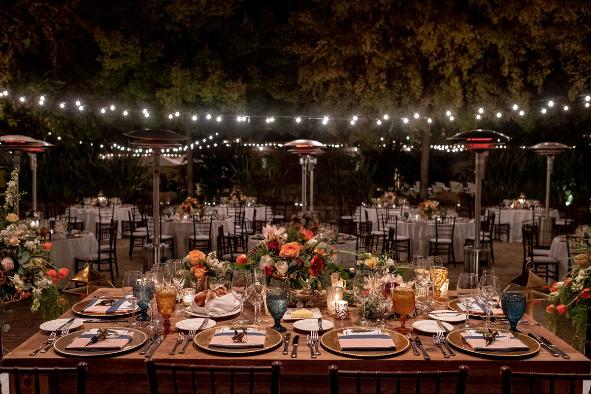San Francisco Bay Area wedding photographer captures romantic evening reception tablescape with autumn floral centerpieces and string lighting under mature trees at Estate Yountville in Napa Valley