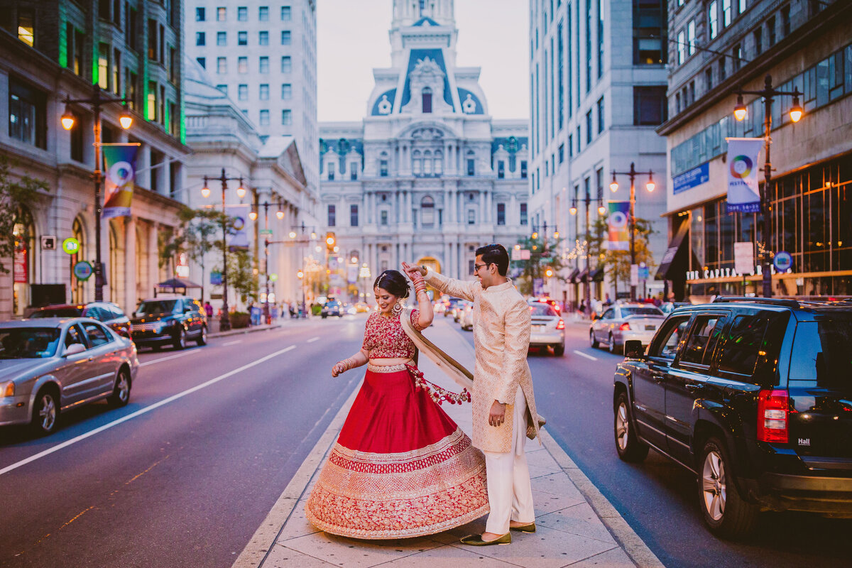 An indian groom twirling the bride on their wedding day before the reception in the evening on broad st in front of the philadelphia city hall