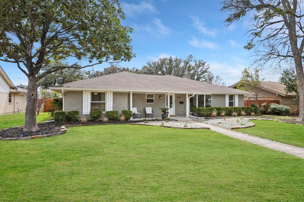 Angled front view of 3120 Chapel Downs Dr, Dallas TX – charming ranch-style home with light brick exterior, covered porch, and mature landscaping, listed by Haven Realty Group.