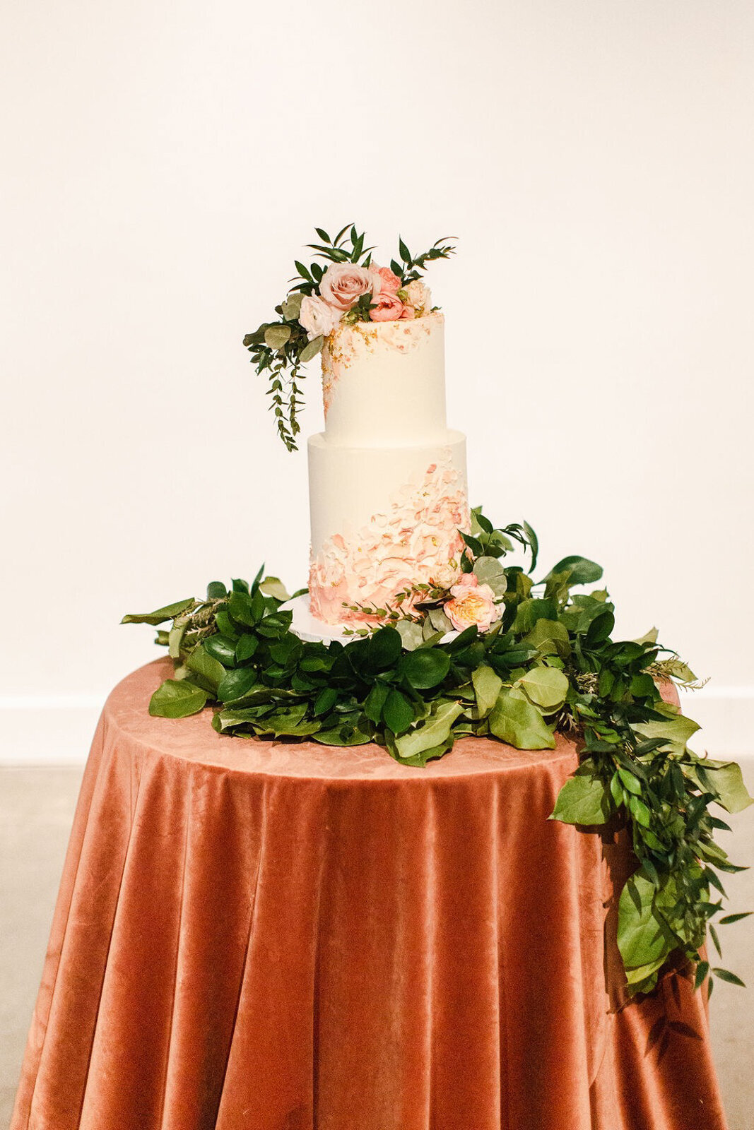 White and peach wedding cake with buttercream textured detail and cascading greenery, created by Bake My Day, contemporary cakes & desserts in Calgary, Alberta, featured on the Brontë Bride Vendor Guide.