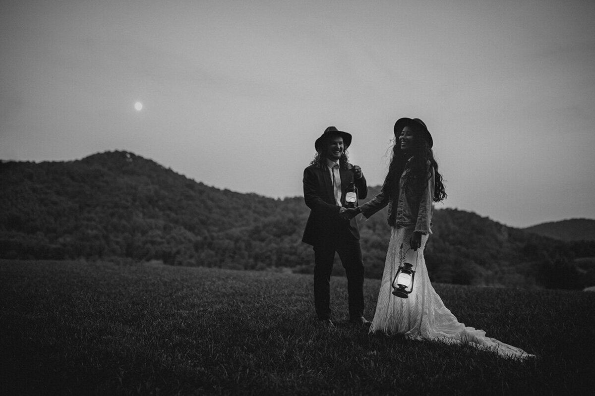 bride and groom pose in the outdoors under the moon light each holding lamps