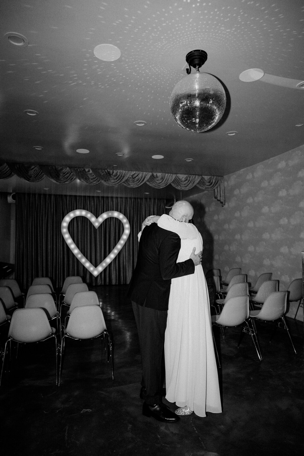 A couple hugs sweetly at their venue under a disco ball.