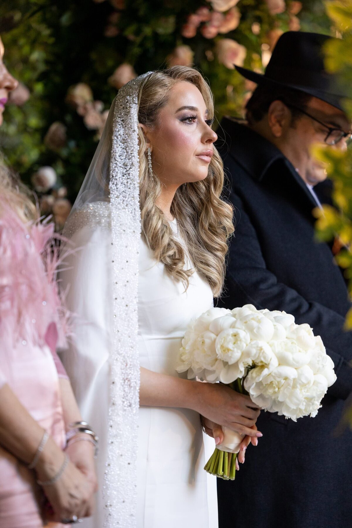 A bride standing with her parents holding a bouquet of flowers