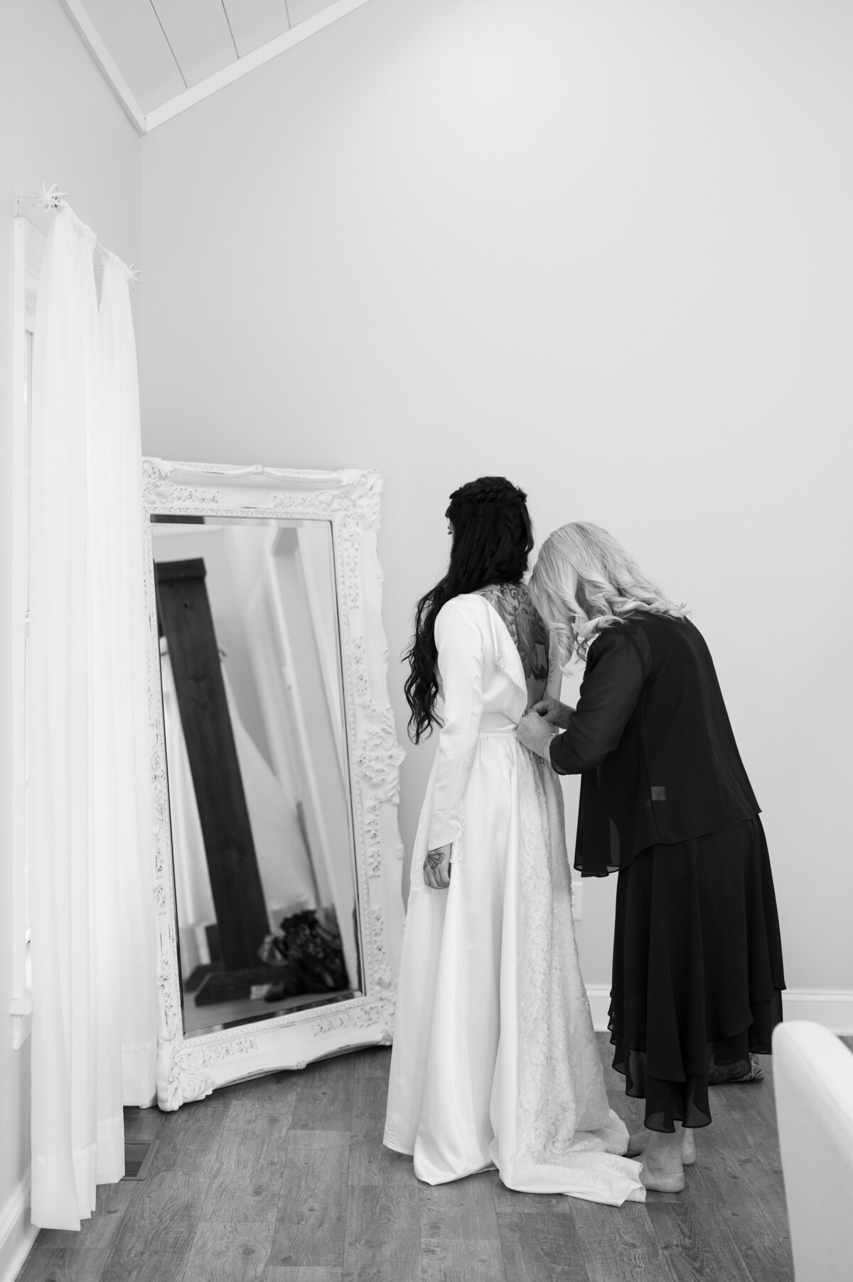 A person helping a bride put on a wedding dress