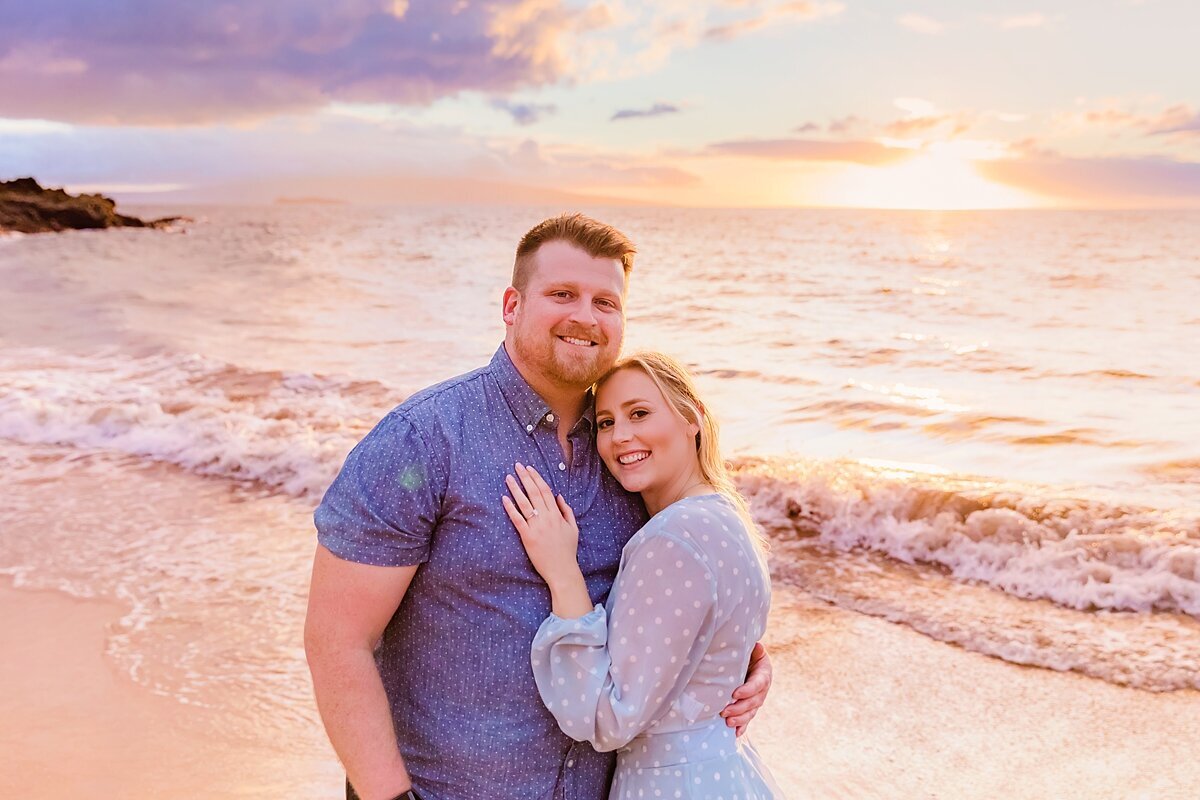 Newly engaged couple smiles at the camera on a beautiful beach during a surprise proposal photoshoot in Wailea