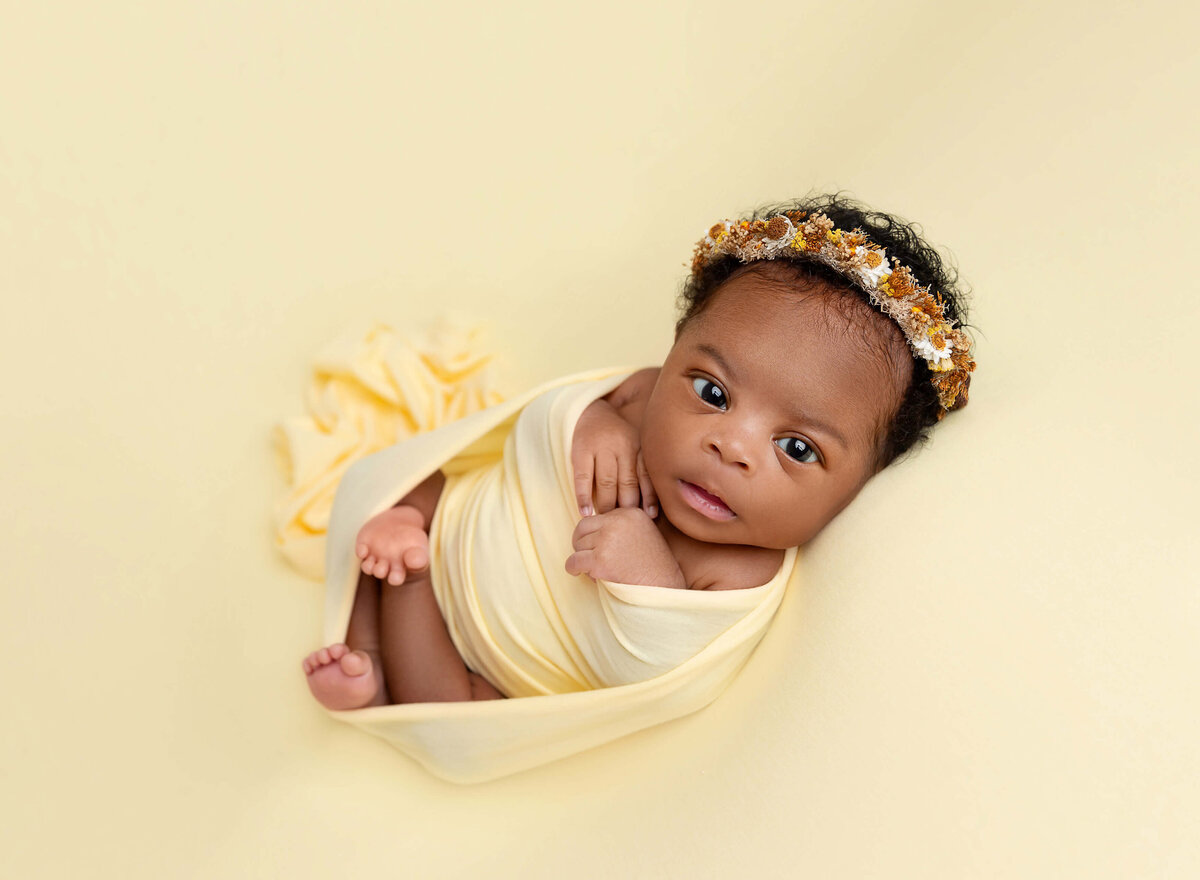 baby girl newborn pictures swaddled in light yellow wrap and laying on the blanket open eye  newborn photosession done by Rochel Konik Photography