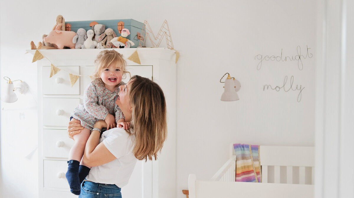 A mum and her little girl cuddle and laugh in her nursery during a family photo shoot