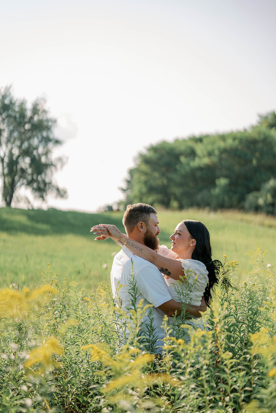 Kali and Joe hugging in tall wildflowers during their engagement session on Detroit private property.