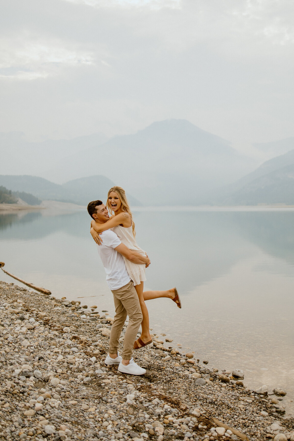 Couple hugging along the waters edge in Kananaskis, Alberta mountains, captured by Love and be Loved Photography, authentic and natural wedding photographer and videographer in Lethbridge, Alberta. Featured on the Bronte Bride Vendor Guide.