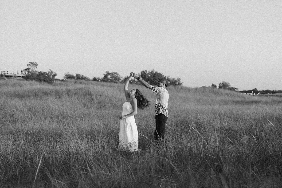 Couple holding hands walking through tall grass at New Buffalo Beach during sunset engagement session