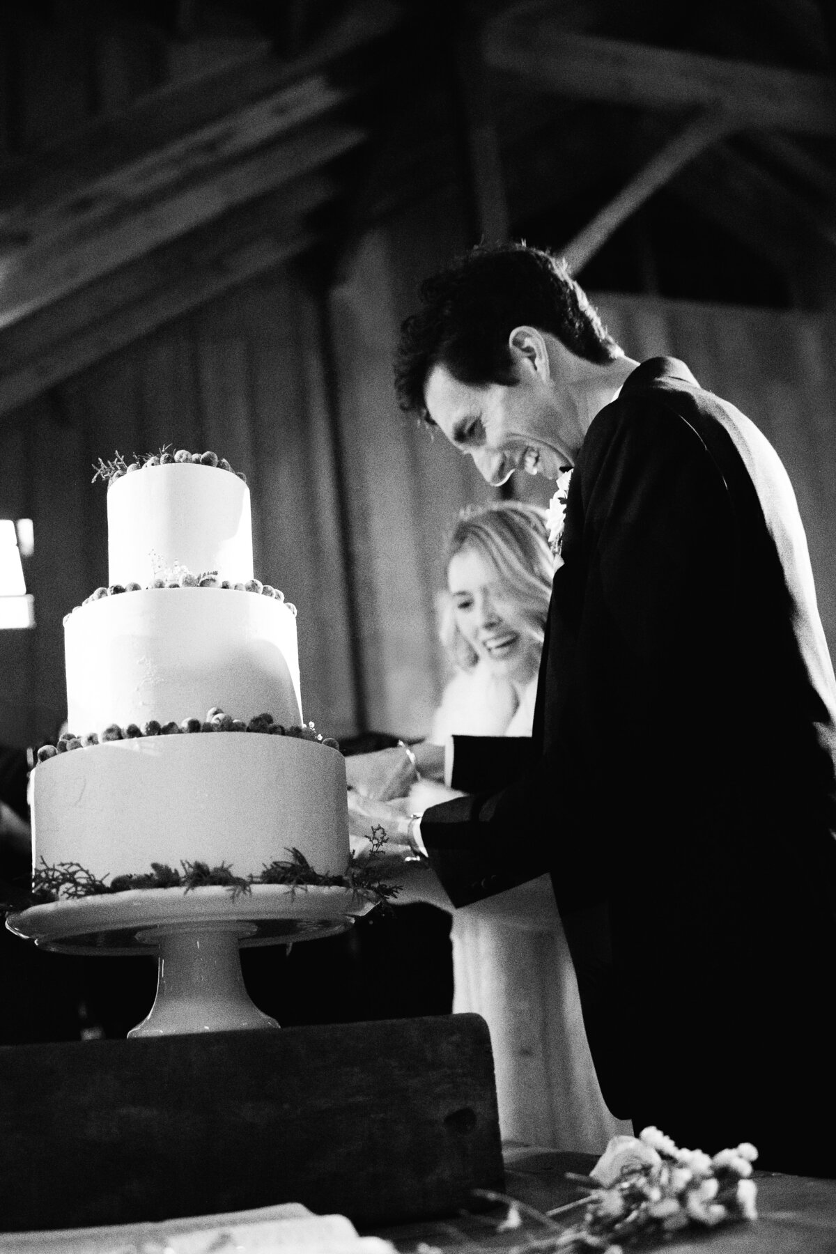 Bride and groom cut their wedding cake in a timeless black and white moment, captured on film by Kate Winters Photography.