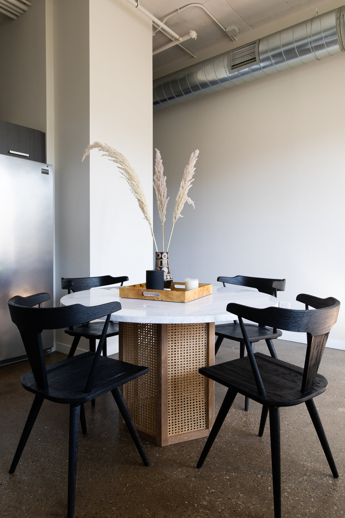 Dining room with concrete floors, round marble dining table with cane base and black wooden chairs