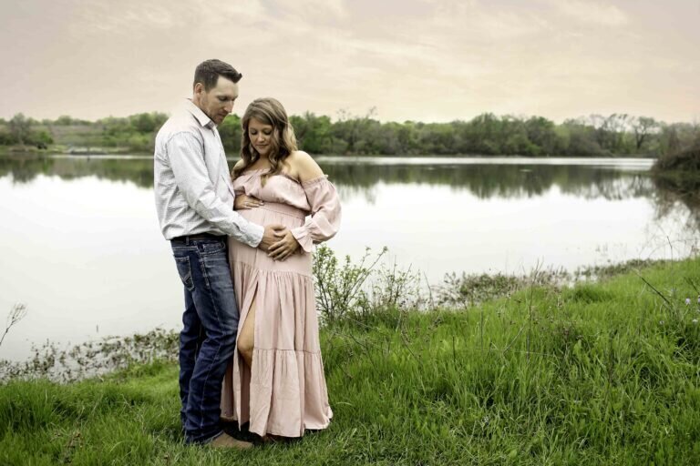 A serene maternity photo of the expectant mom and dad standing hand-in-hand by the lake, with the calm water reflecting the couple's love and excitement, beautifully captured by Chunky Monkey Photography.