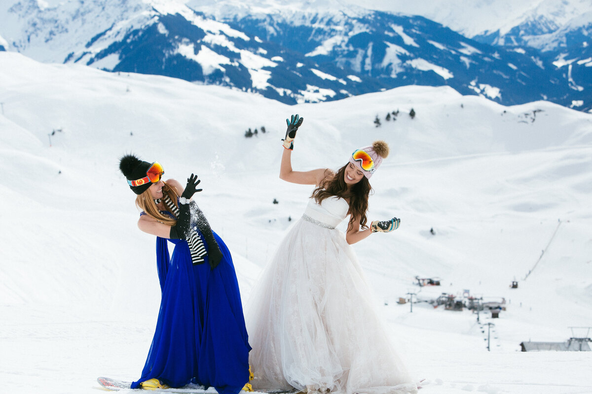 Bride, groom, and friends laughing in snow with snowboards and goggles – après-wedding energy in Kitzbühel by Studio Rose