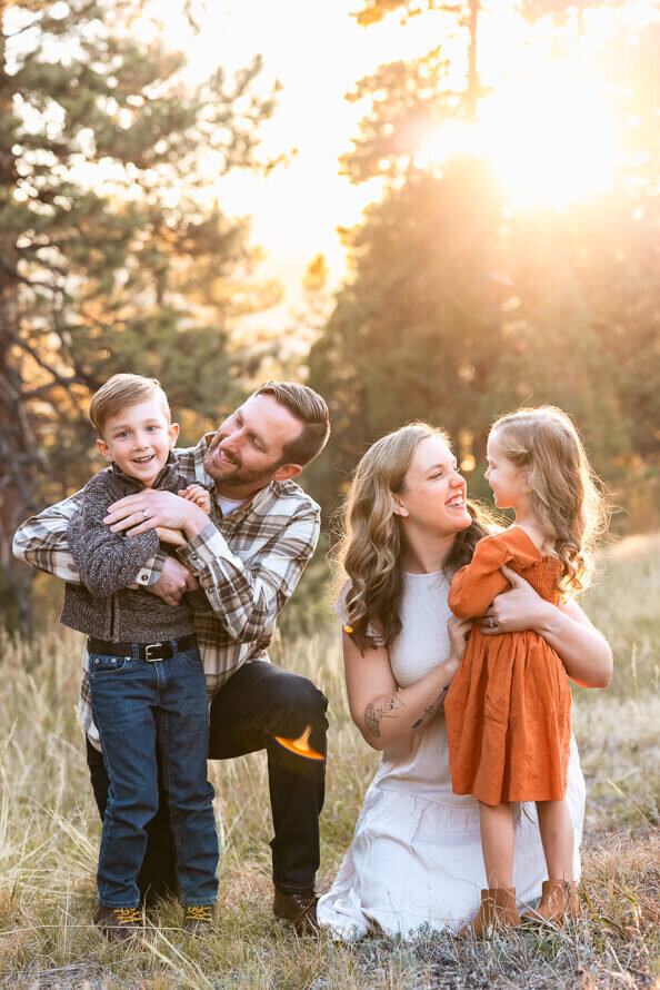 Mom and dad tickle two small kids with the sunlight pouring onto them.