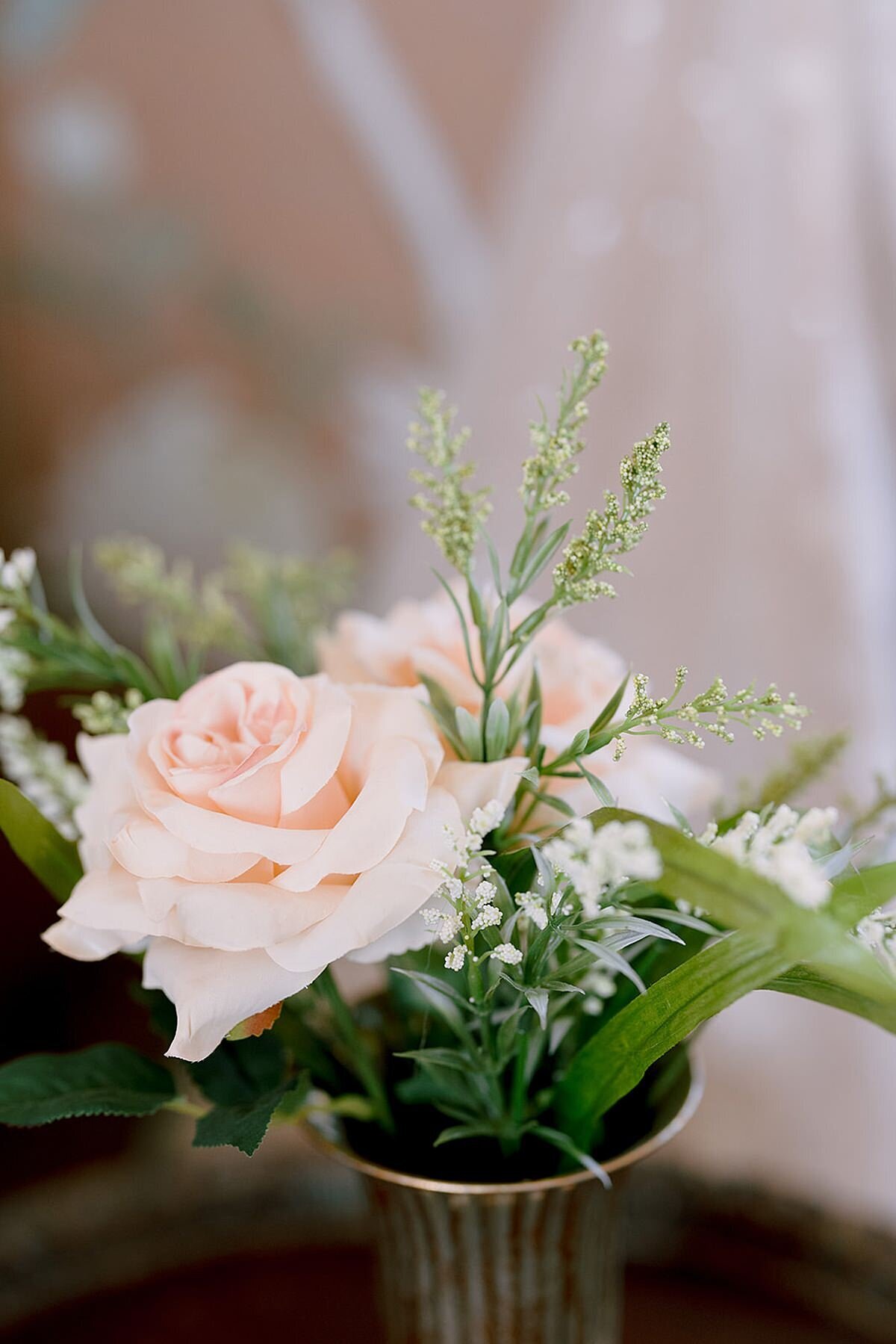 Pink roses with small white flowers and greenery in a small fluted antique silver vase for a cocktail table.