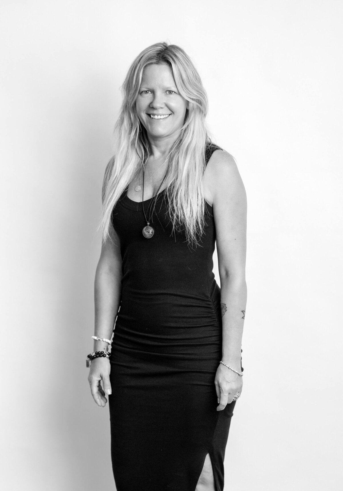Before shot of a woman wearing an Adidas tank top, standing against a white background with a natural smile.