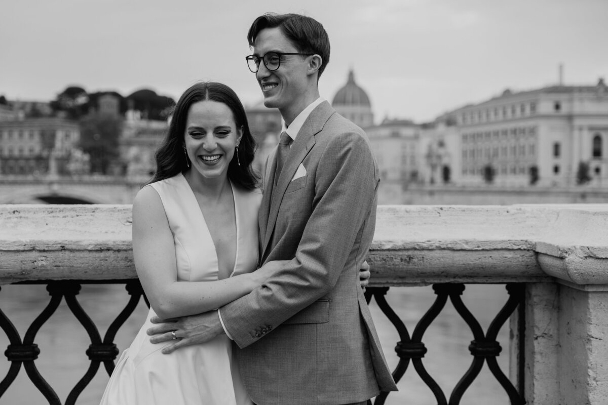Couple embracing on a bridge overlooking Rome.