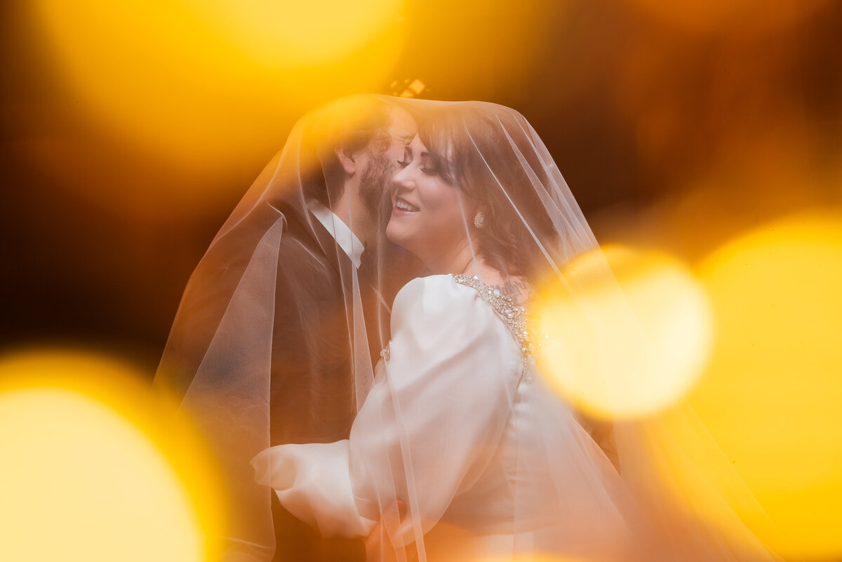 Nighttime-portrait-of-bride-and-groom-with-orange-bokeh-balls-in-foreground-at-Asheville-Masonic-Temple