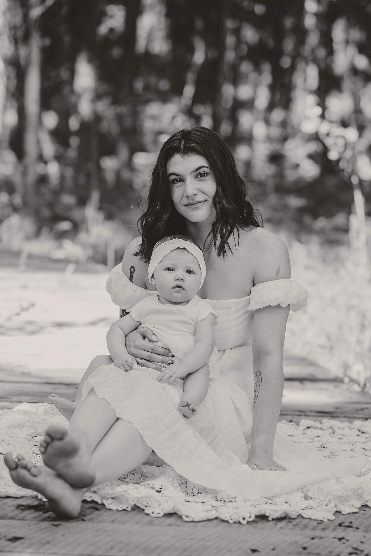 A mother sits on a wooden bridge with herinfant daughter in her lap. Captured by Brittany Danielle.