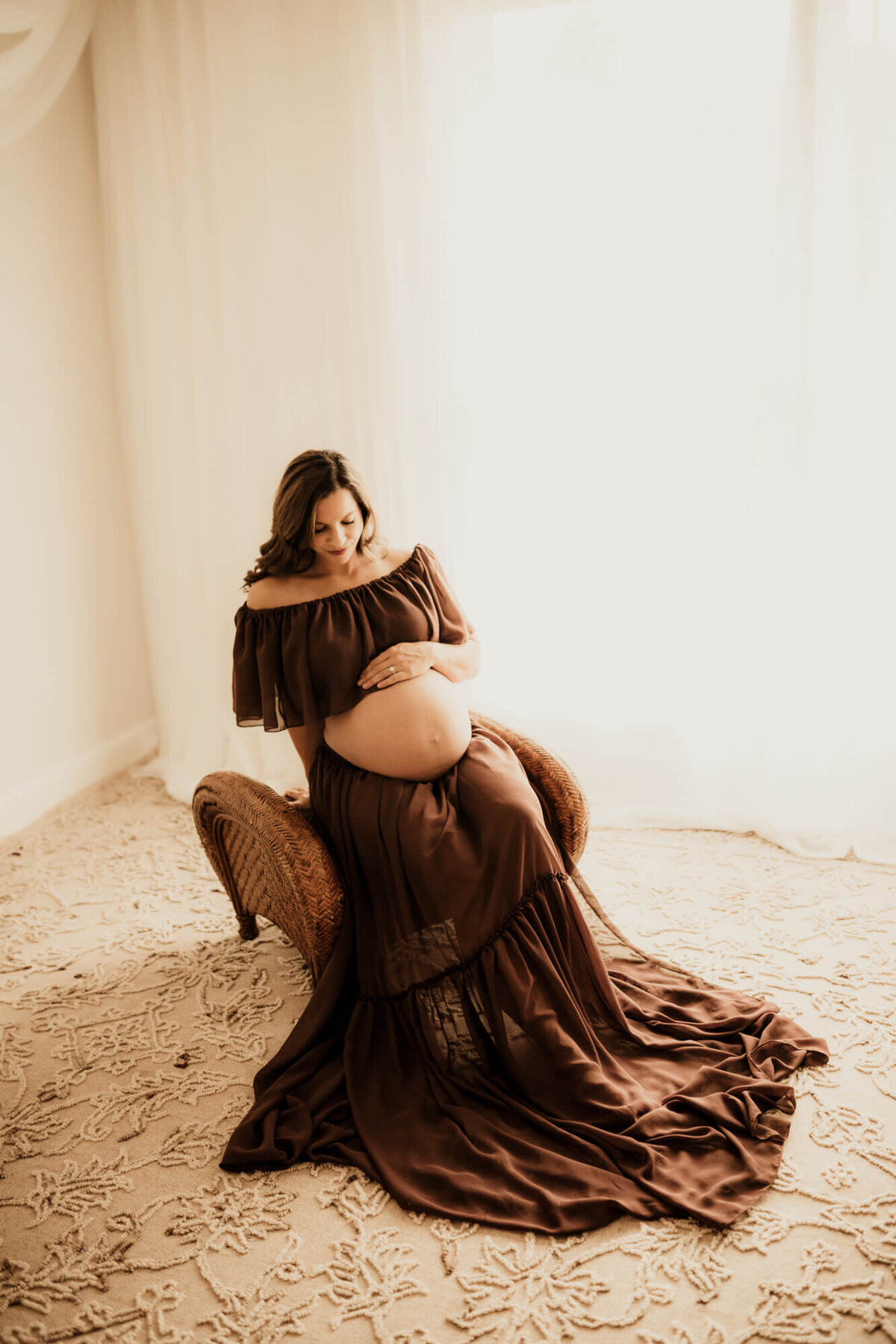 Mother in her third trimester looking at her baby bump while sitting on an ottoman.