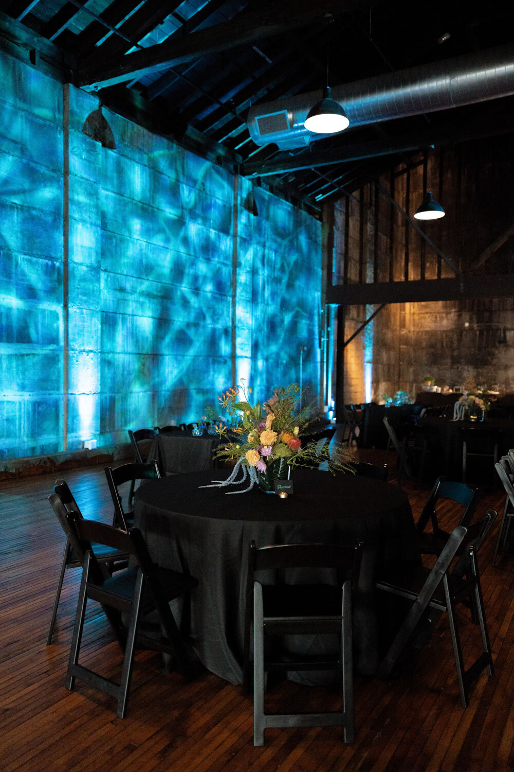 Dimly lit event space with black table settings and blue wall lighting