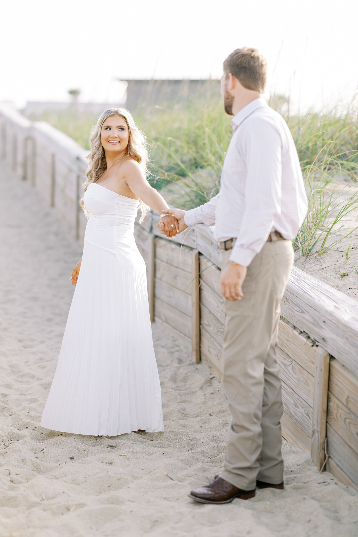 engaged couple walking on the beach beside a wooden fence