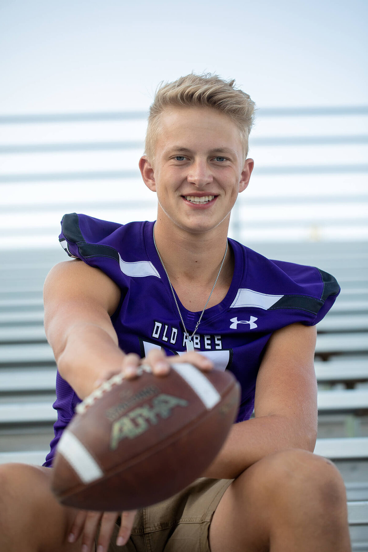 Senior boy in his Memorial football jersey holding out a football.