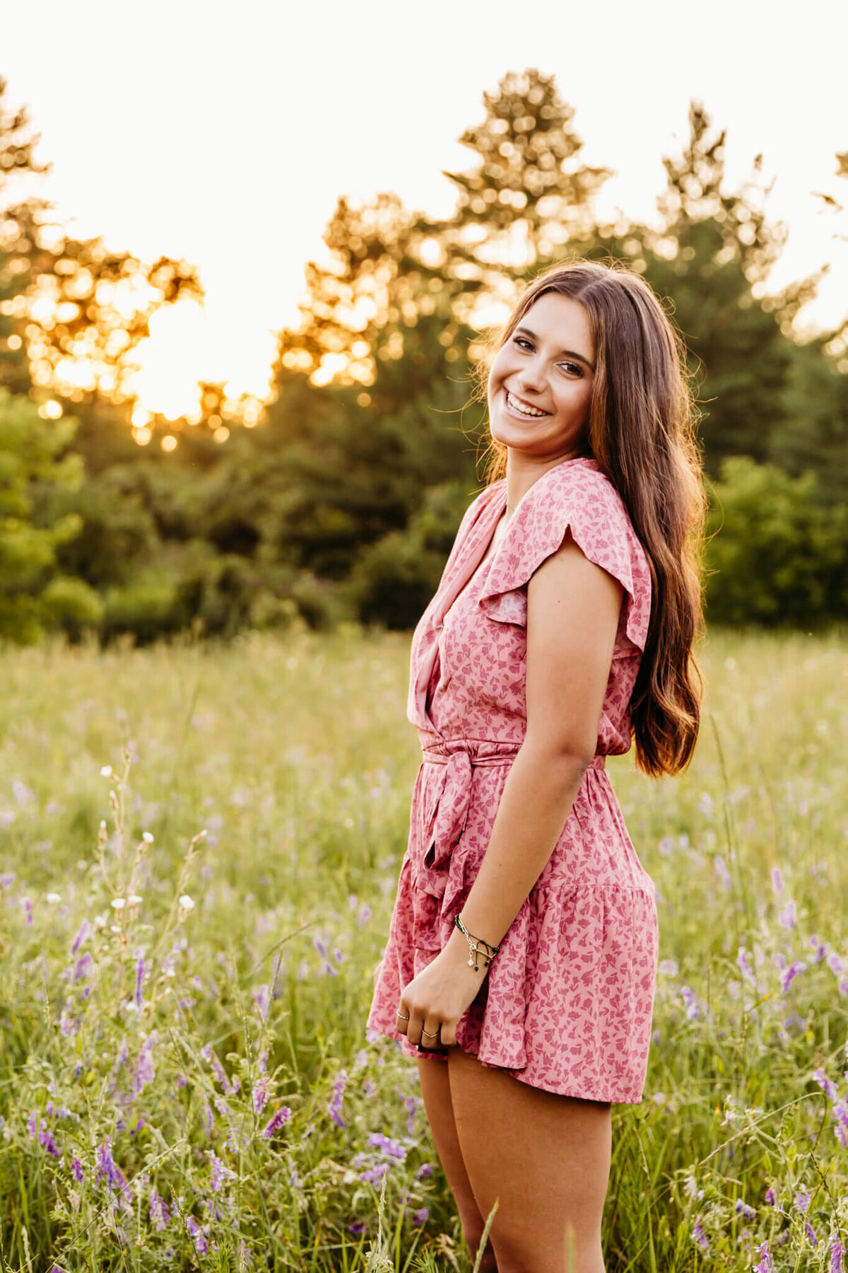 high school senior girl laughing as she stands in a field full of purple and white flowers at sunset