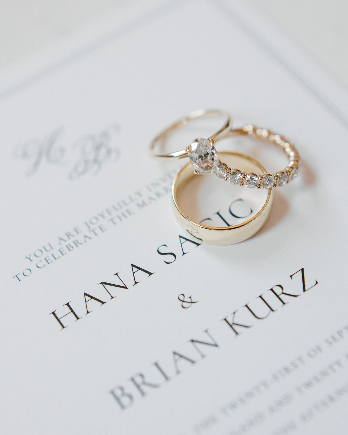 Engagement and wedding rings resting on a printed invitation with names “Hana Sasic & Brian Kurz,” styled in Philadelphia.
