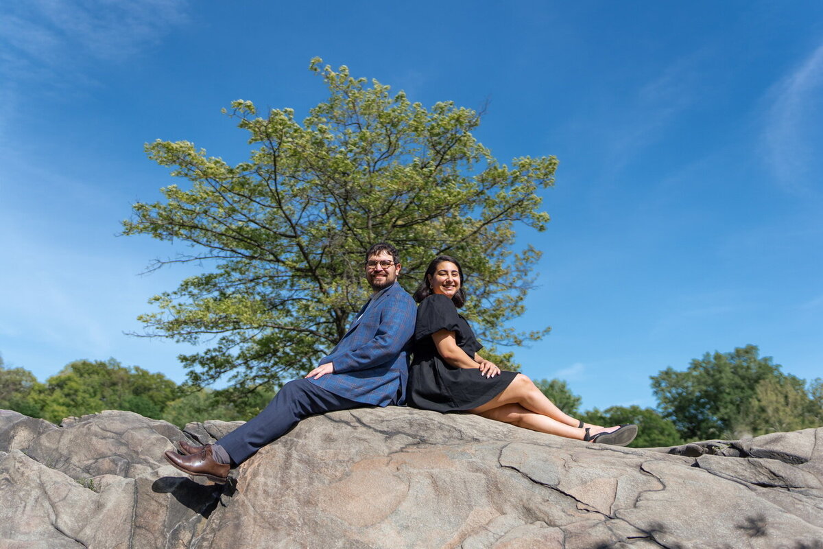 straight mixed race couple sit and pose on a rock in Central Park