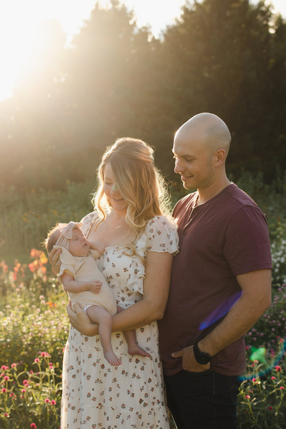 Hudson Valley Newborn Photographer captures a tender family moment with parents smiling at their newborn in a blooming field.