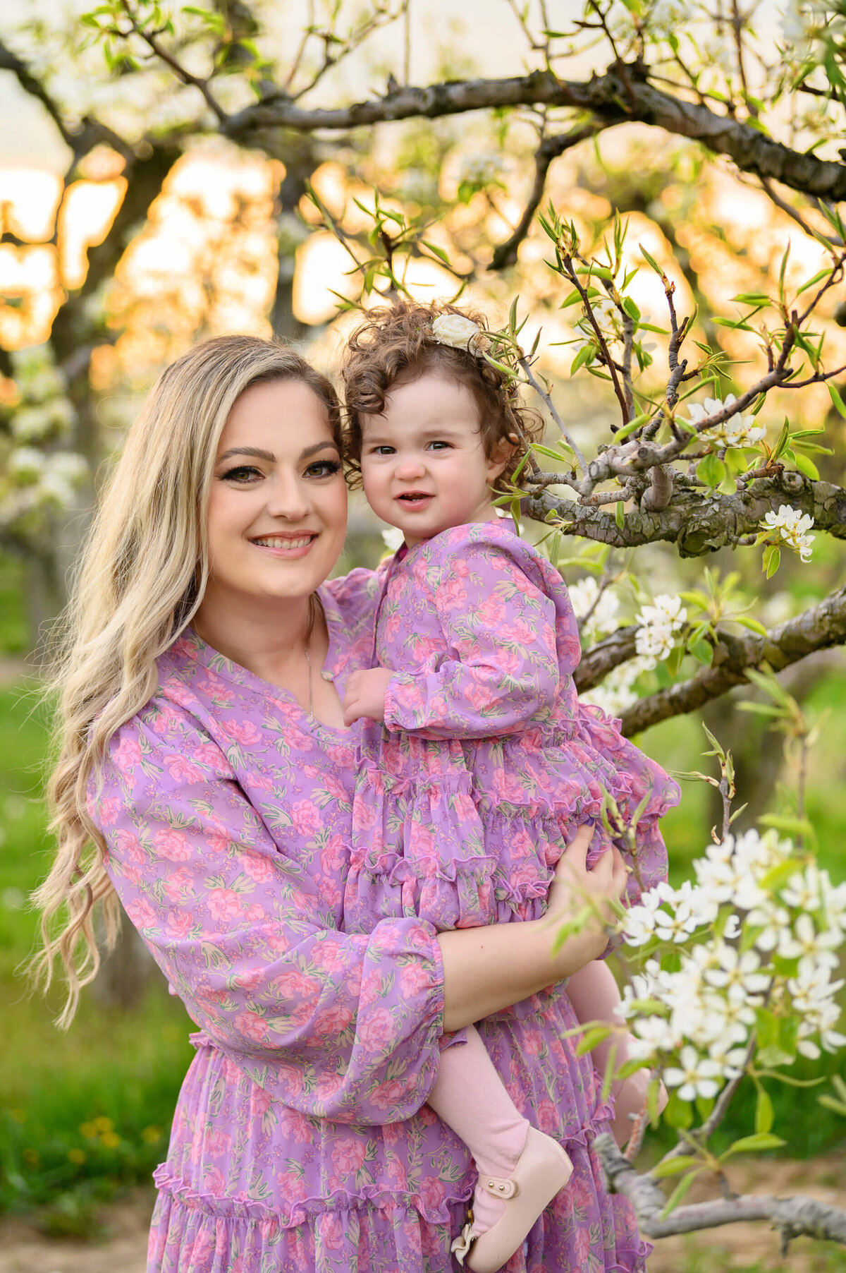 mom holding her daughter both wearing purple in the white cherry blossom field for their family photographer session in Burlington, On
