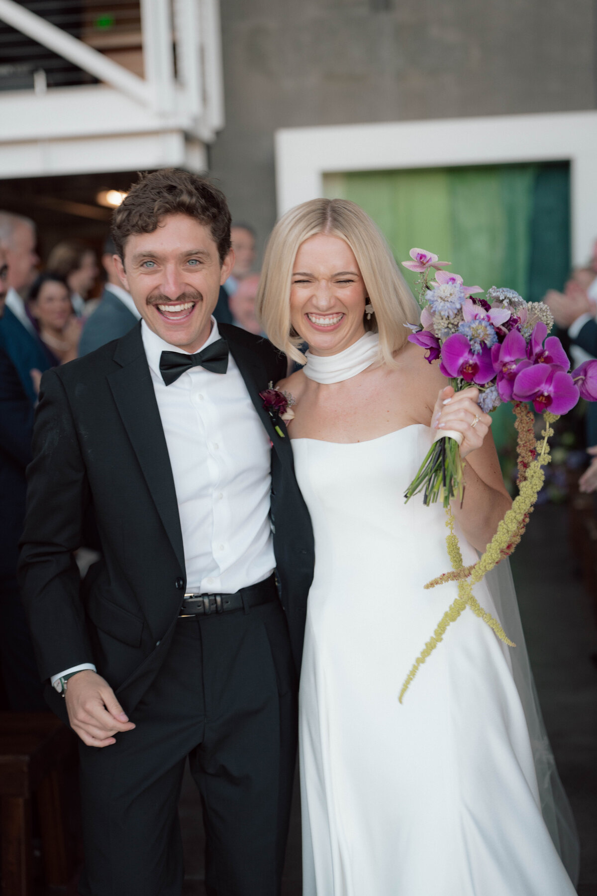 Bride and groom laughing together after wedding ceremony holding bouquet