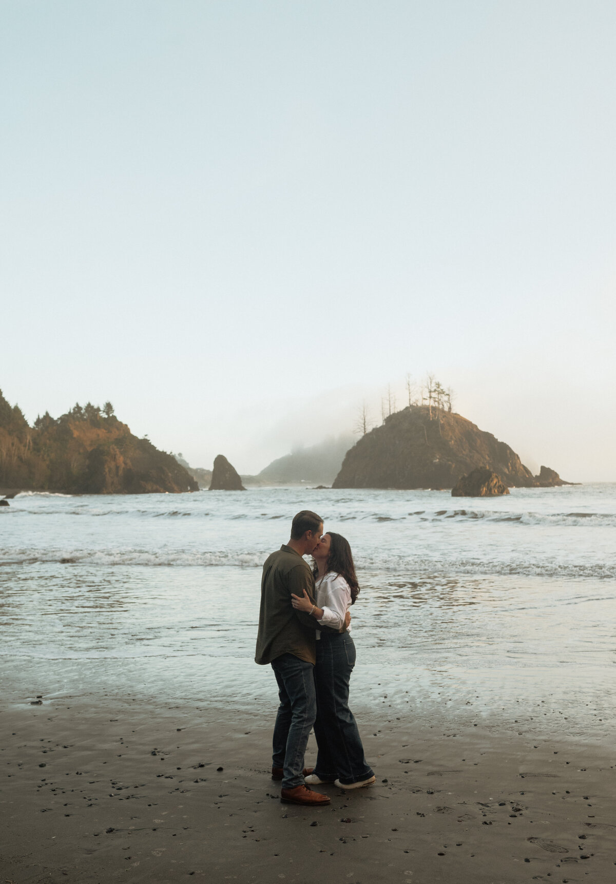 intimate engagement session with couple gazing at each other while standing in front of crashing waves
