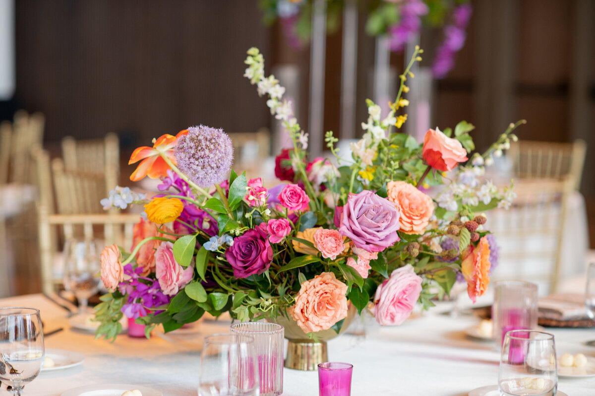 Vibrant table centerpieces in sunset hues of lavender, orange, rosy pink, and golden-yellow composed of roses, garden roses, allium, orchids, delphinium, and ranunculus. Design by Rosemary and Finch in Nashville, TN.