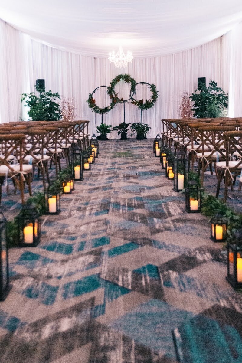 Indoor wedding ceremony featuring candles, greens, and floral installation.