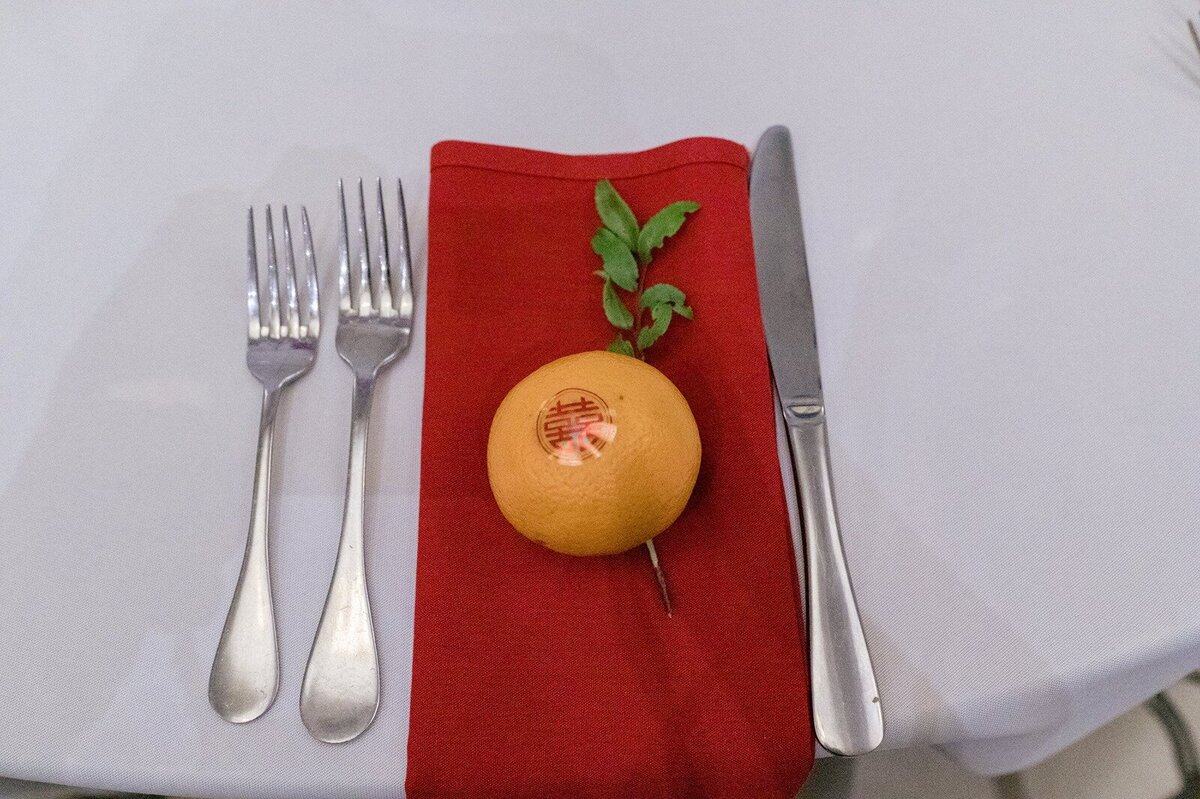 Simple and modern wedding table decor featuring red napkin, vibrant greenery and orange accent.