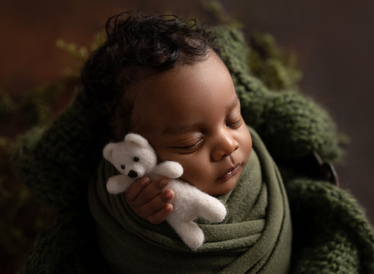 Close-up of newborn boy swaddled in green holding tiny white felt teddy bear | Austin newborn photographer serving Georgetown and surrounding areas