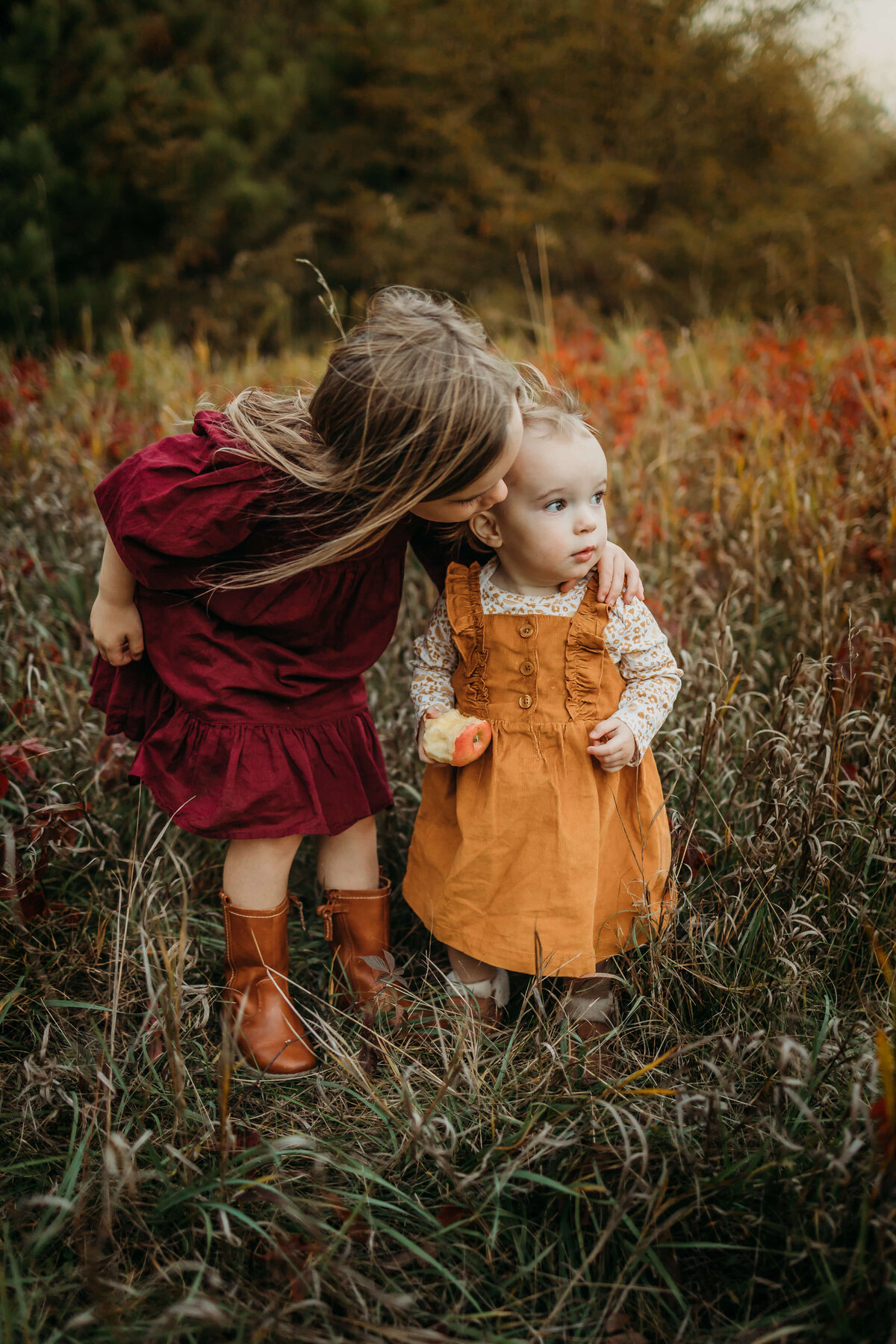 big sister kissing little sister on head outside fall colors