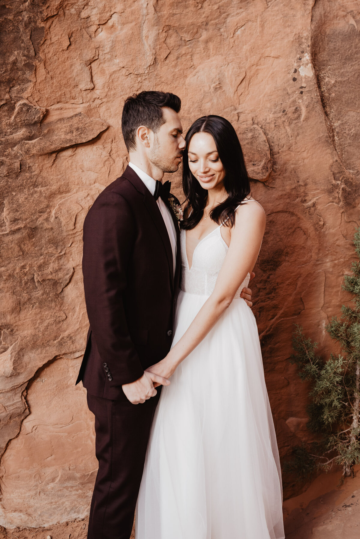 utah elopement photographer captures bride and groom hugging while man wears burgundy suit