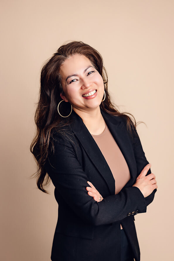 Woman folds arms and laughs in tan studio.