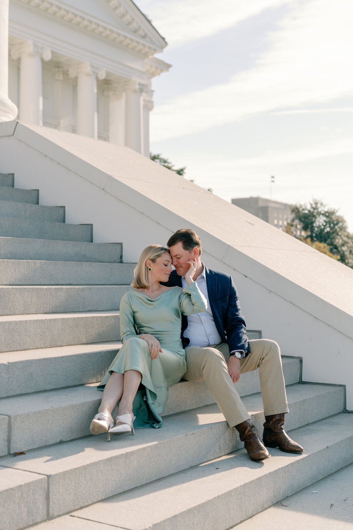 Virginia Capitol Building Engagement Session Richmond VA | couple in green dress and blue suit sit on the grand white staircase of the Virginia Capitol