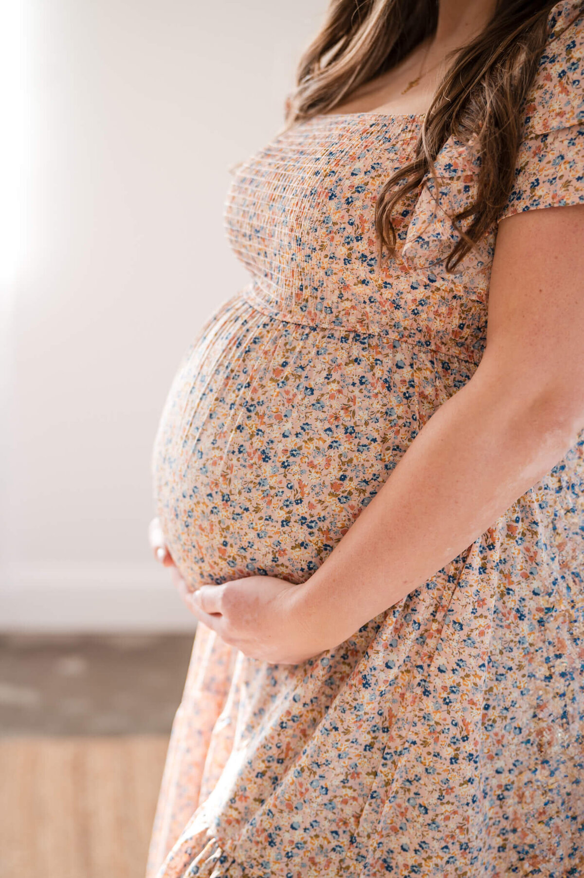 Woman holding pregnant belly in floral dress in Studio Neue