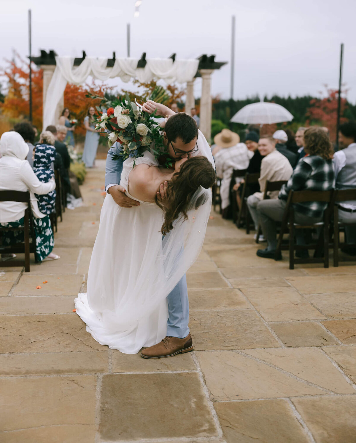 A groom leans a bride in a back bend as they embrace and kiss celebrating their marriage.