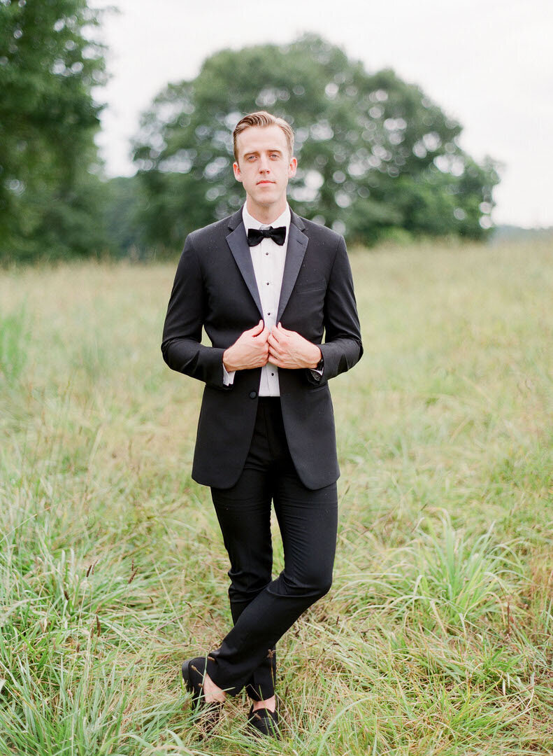 Groom in Field Buttoning Jacket at The Inn at Serenbe Wedding Photo